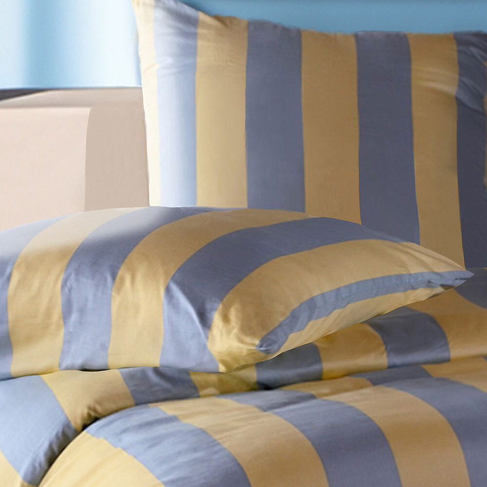 Modern Life Streifen Bettwäsche. Ein Bett, das mit gestreifter Bettwäsche in gelb und blau bezogen ist. Im Hintergrund ist eine hellblaue Wand. Die Bettwäsche wurde vom nahen fotografiert.