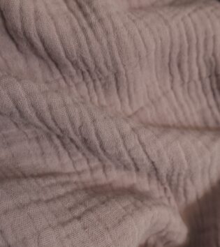 Nahaufnahme von strukturiertem Musselin-Stoff in mauve, mit sichtbarer Crinkle-Oberfläche.